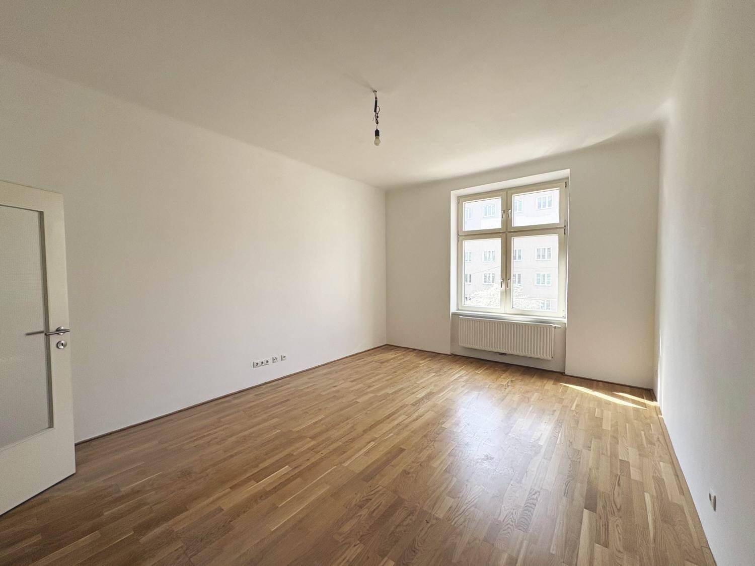 Geräumiger, unmöblierter Raum mit Holzparkett und einem Fenster, das den Blick nach draußen freigibt.