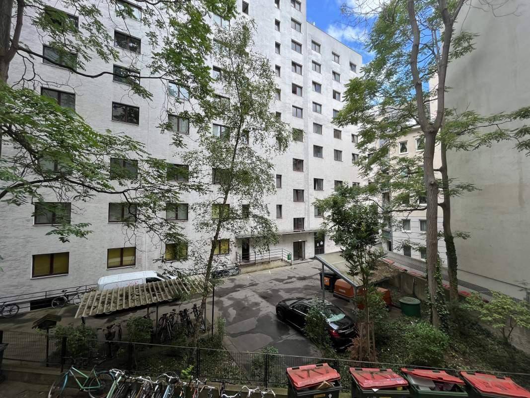 Innenhof mit Parkplätzen und Bäumen, umgeben von einem mehrstöckigen Wohngebäude.