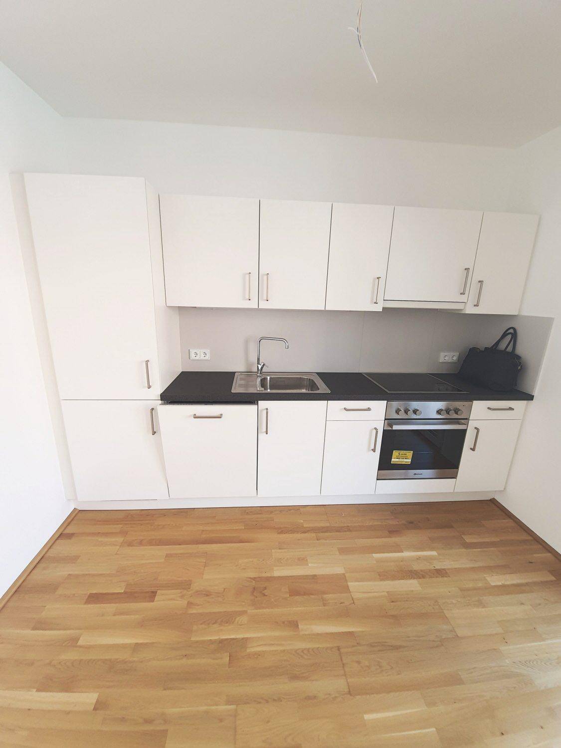 Moderne Küchenzeile mit weißen Schränken, dunkler Arbeitsplatte und integriertem Backofen.