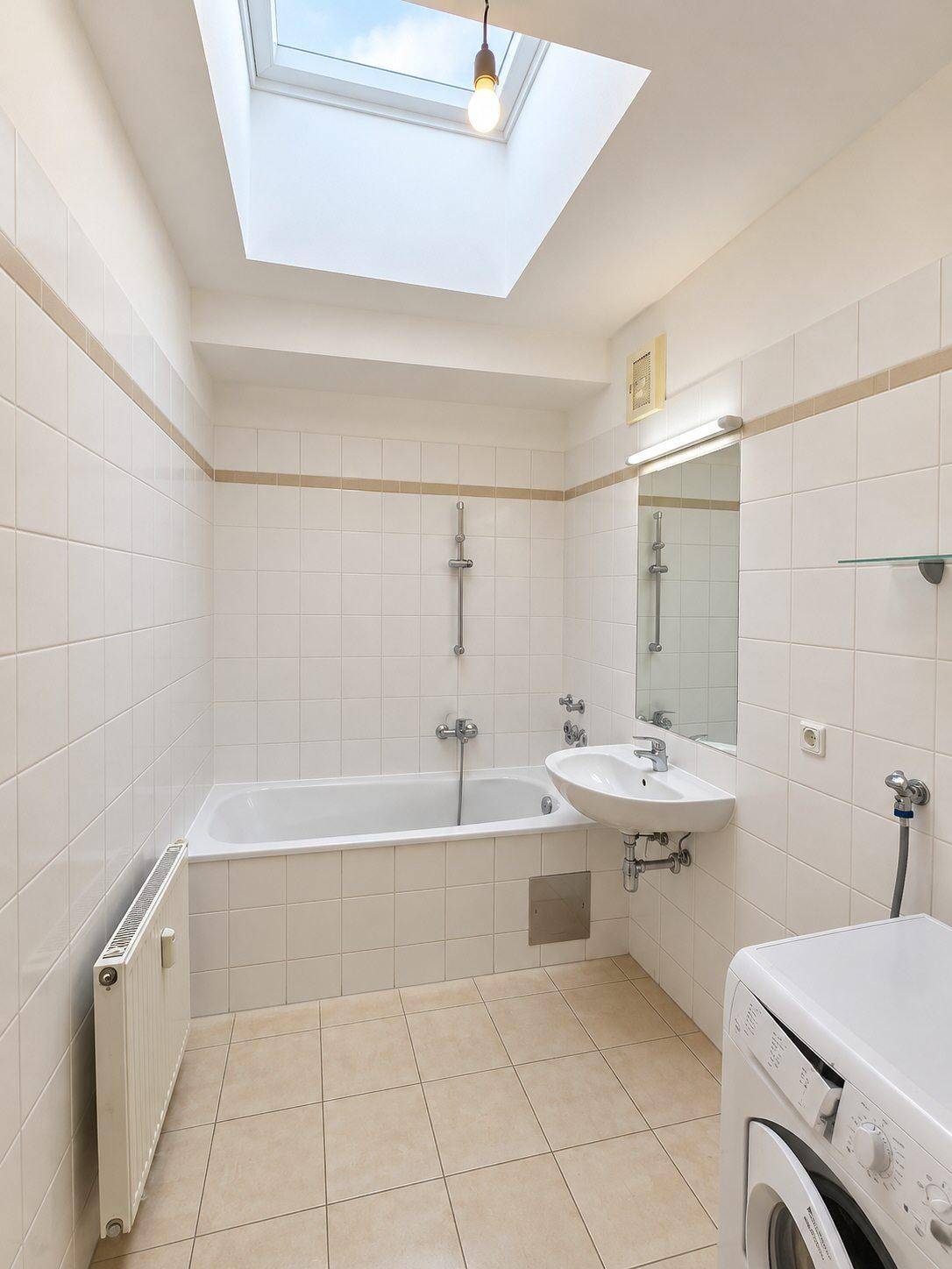 Gefliestes Badezimmer mit Badewanne, Waschbecken, Waschmaschine und einem praktischen Dachfenster.