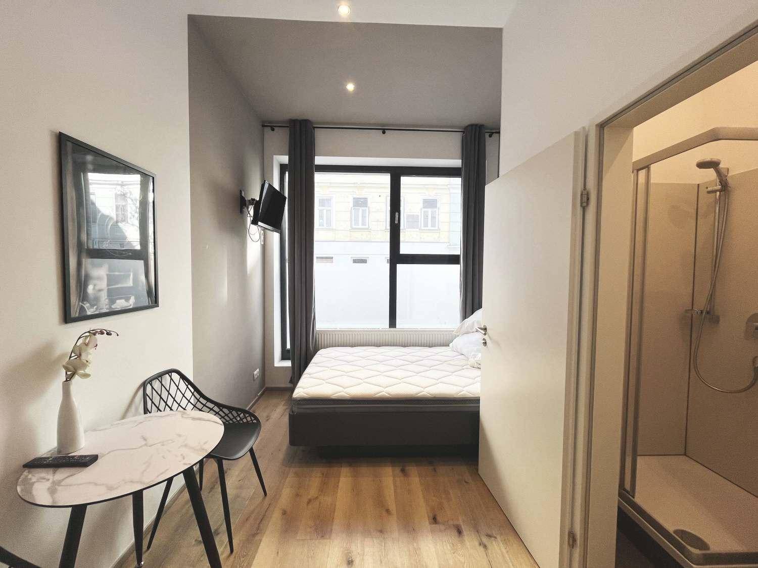 Helles Schlafzimmer mit großem Fenster, Holzboden und direktem Zugang zu einer Duschkabine.