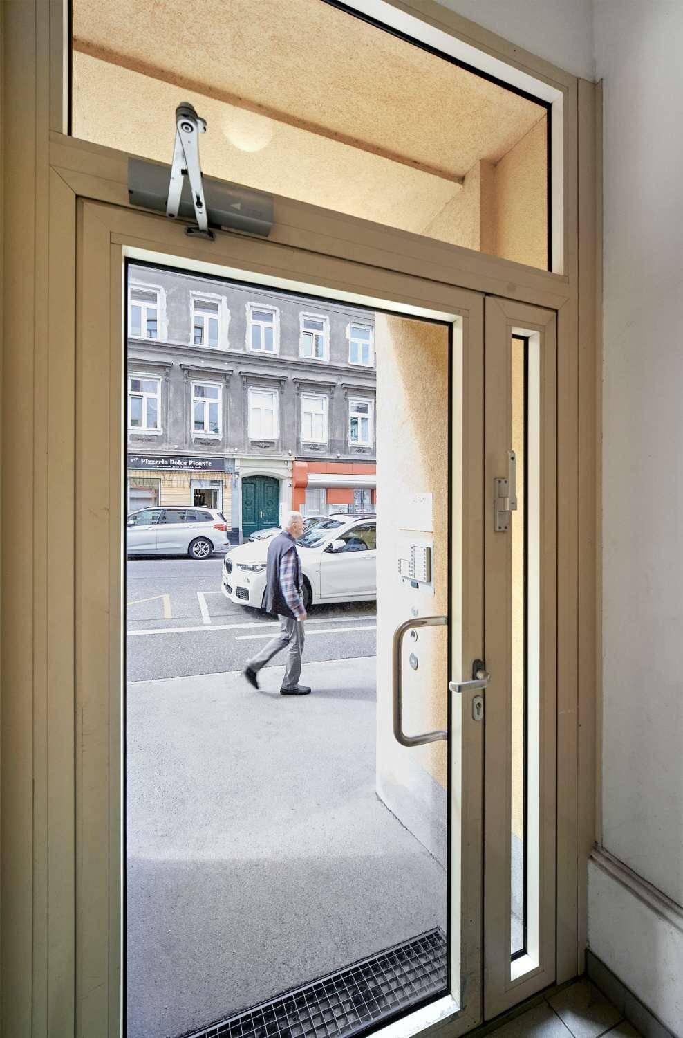 Blick durch eine Glastür aus einem Eingangsbereich auf die Straße mit einem Passanten.