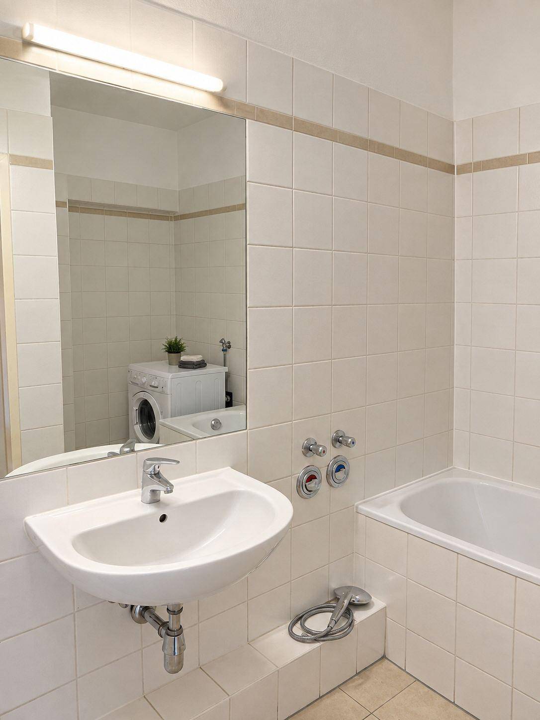 Badezimmer mit Waschbecken, großem Spiegel und Badewanne, die eine Waschmaschine beherbergt.