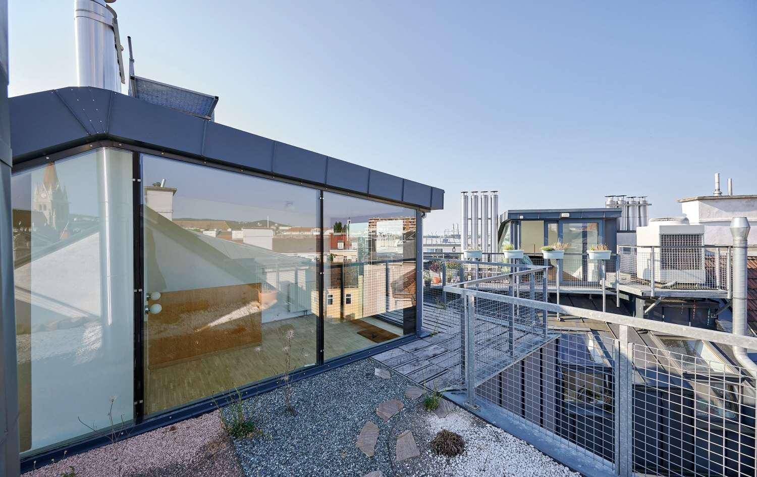 Dachterrasse mit Kiesbereich, Metallgeländer und weitem Blick über die Dächer der Stadt.