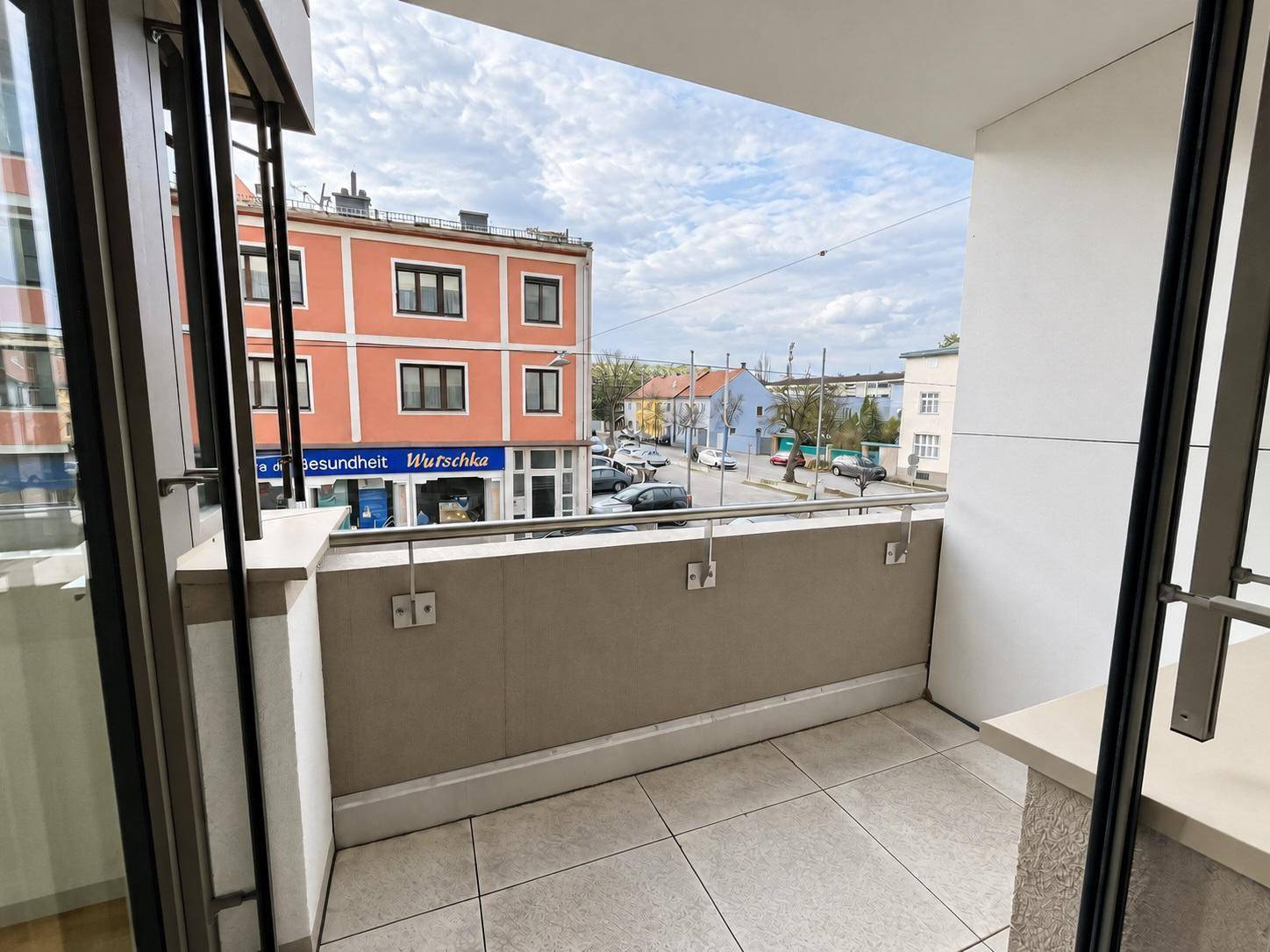 Balkon mit Fliesenboden und Blick auf die belebte Straße und umliegende Gebäude.
