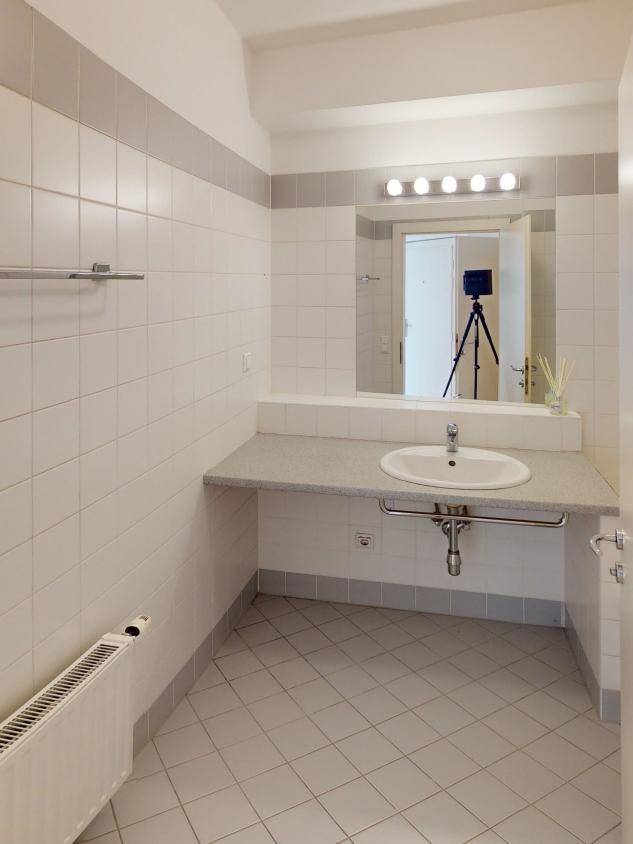 Badezimmer mit weißen und grauen Fliesen, Einzelwaschbecken und großem Spiegel mit Beleuchtung.