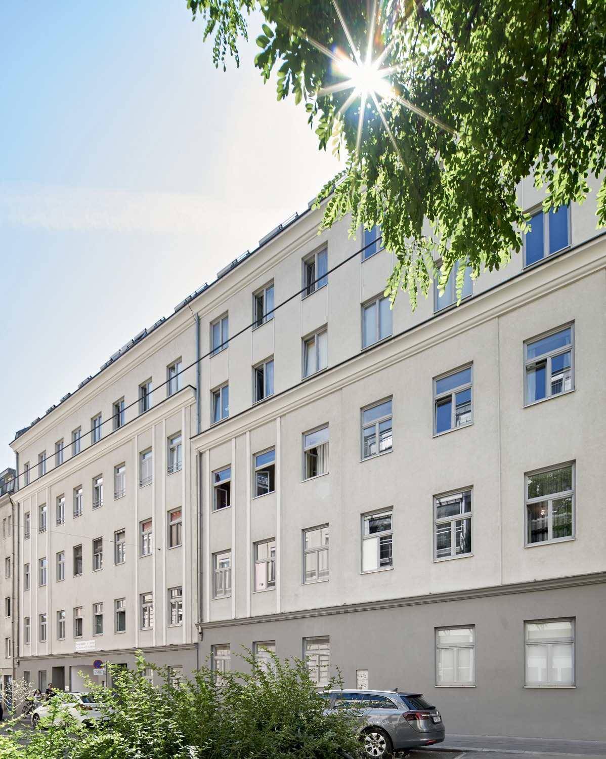 Sonnenbeschienene Fassade eines modernen Wohngebäudes mit vielen Fenstern und grüner Umgebung.