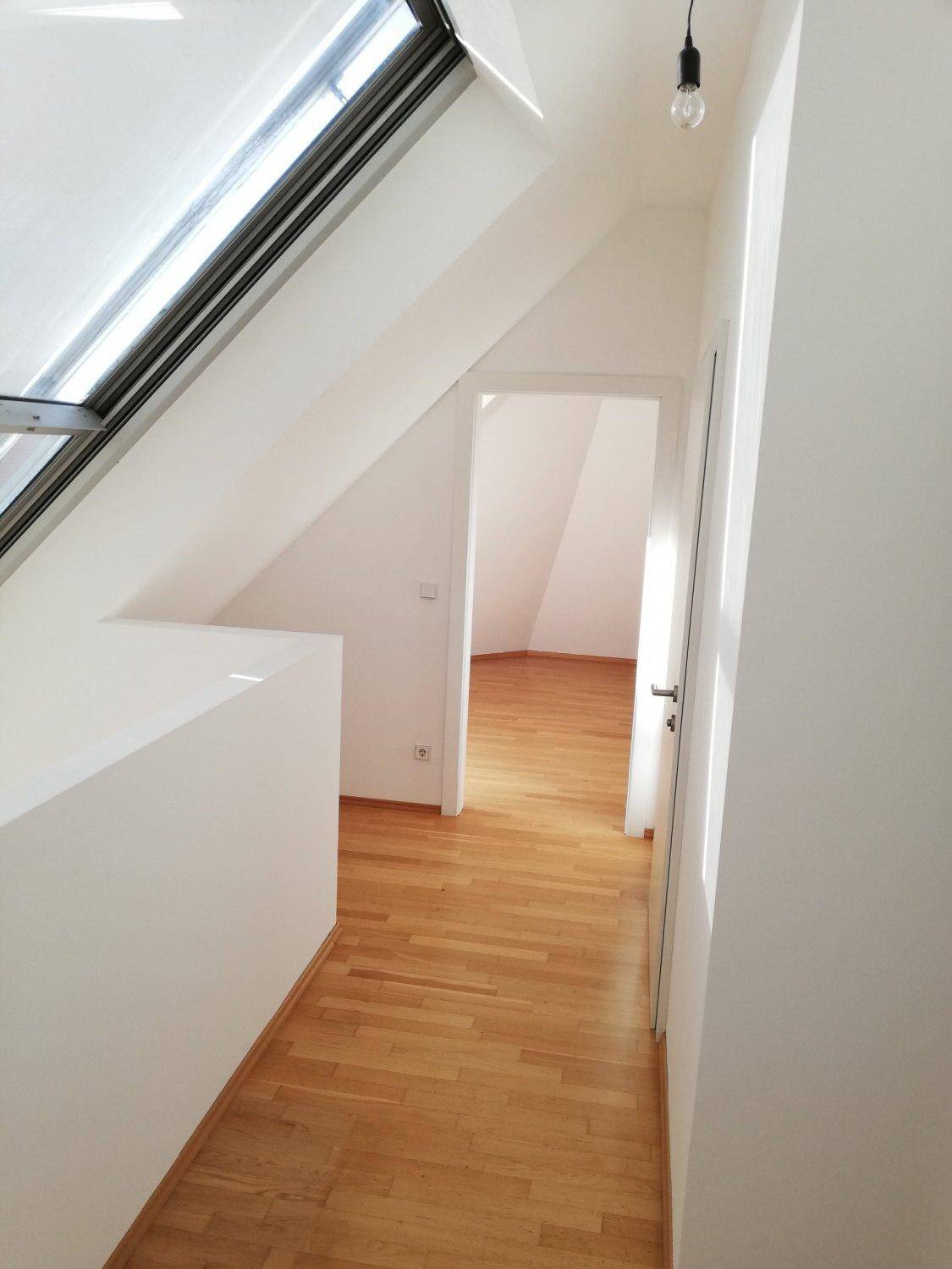 Heller Flur im Dachgeschoss mit Holzboden, Dachfenster und Zugang zu weiteren Räumen.