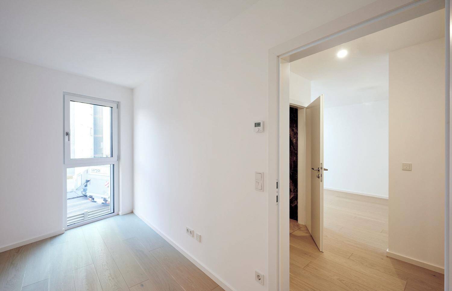 Leeres Zimmer mit hellem Parkettboden und Zugang zu einem kleinen Balkon.