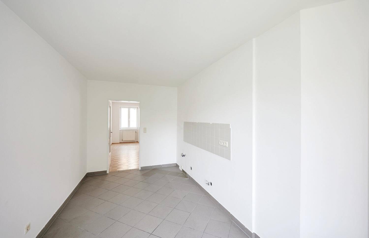 Geräumiger Küchenbereich mit grauen Fliesen und vorbereiteten Wänden für die Installation einer Küche.