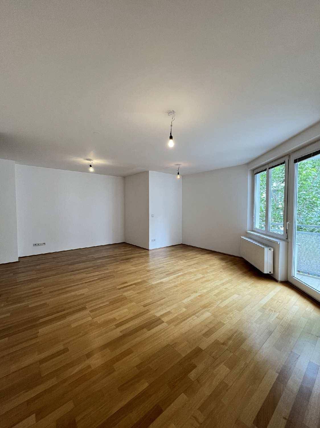 Geräumiges Wohnzimmer mit hellem Parkettboden und großem Fenster mit Balkonzugang.