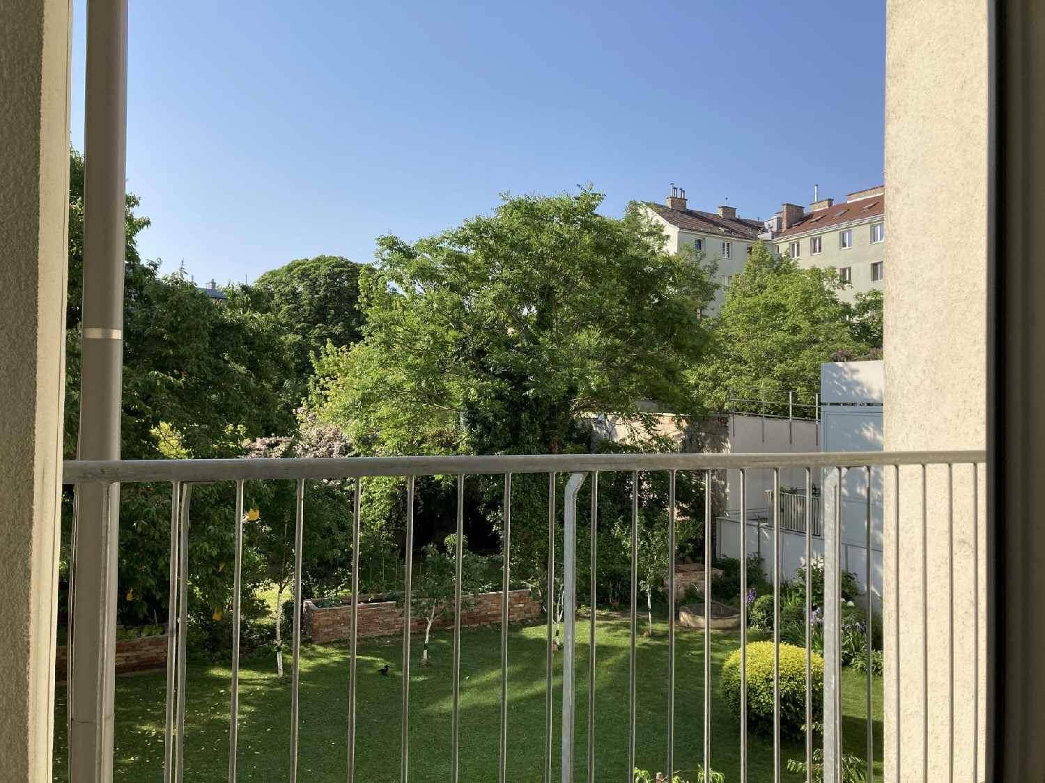 Grüner Ausblick von einem Balkon auf einen gepflegten Garten und umliegende Gebäude.