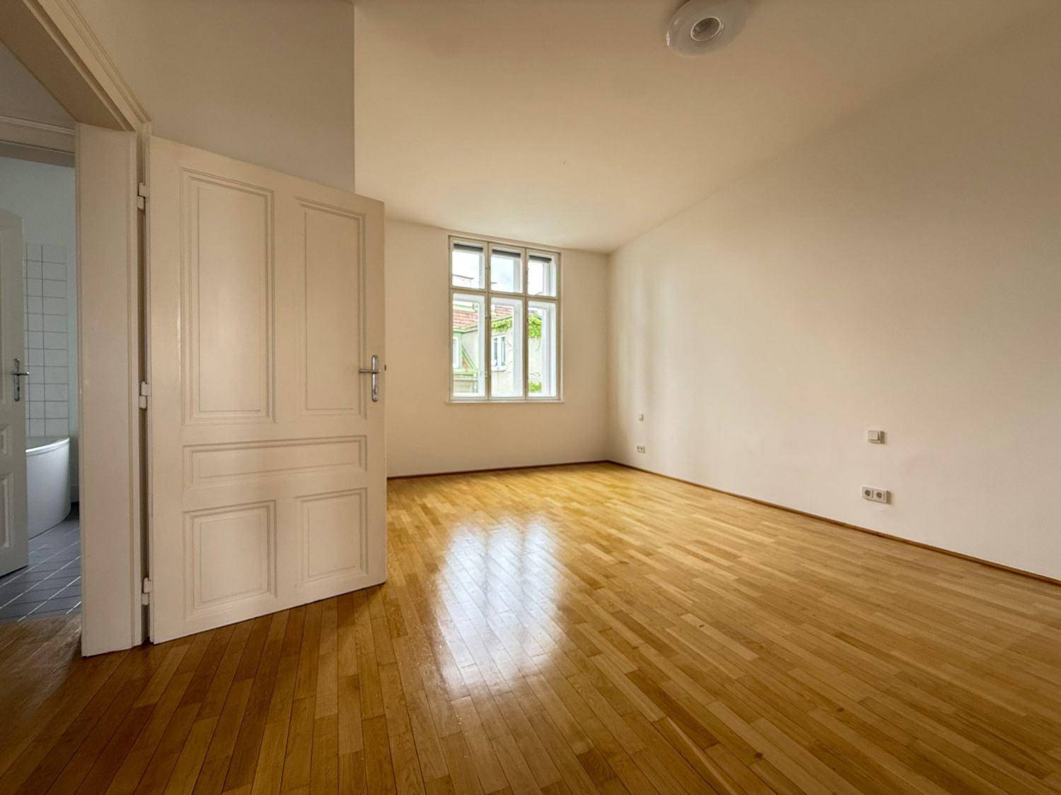 Leeres Zimmer mit hellem Parkettboden und großem Fenster, bereit zur individuellen Gestaltung.