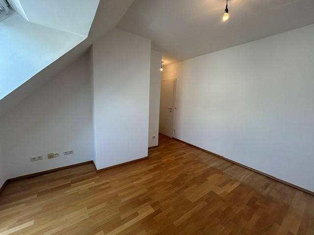 Ruhiges Zimmer mit Parkettboden, weißen Wänden und Dachschräge.