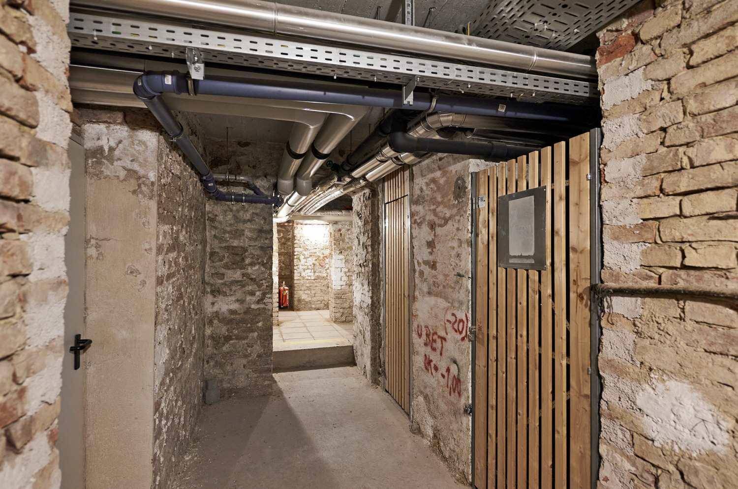Historischer Kellerraum mit unverputzten Ziegelwänden und sichtbaren Leitungen.