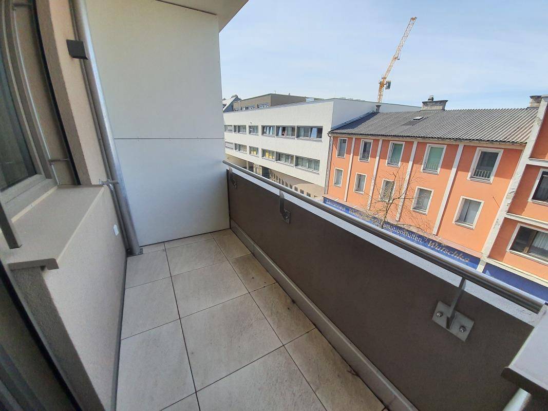 Schmaler Balkon mit Fliesenboden und Blick auf die umliegende Stadtbebauung.