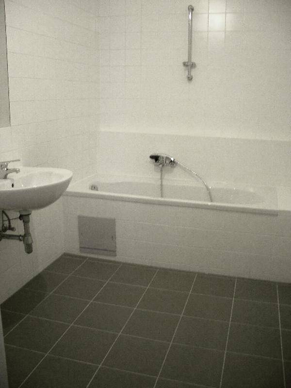 Badezimmer mit weißer Badewanne und Waschbecken, ausgestattet mit grauen Bodenfliesen.