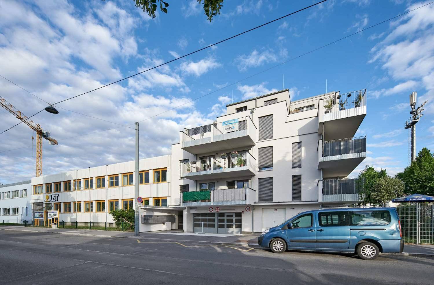 Modernes Wohngebäude mit Balkonen und Tiefgaragenzufahrt in städtischer Umgebung.