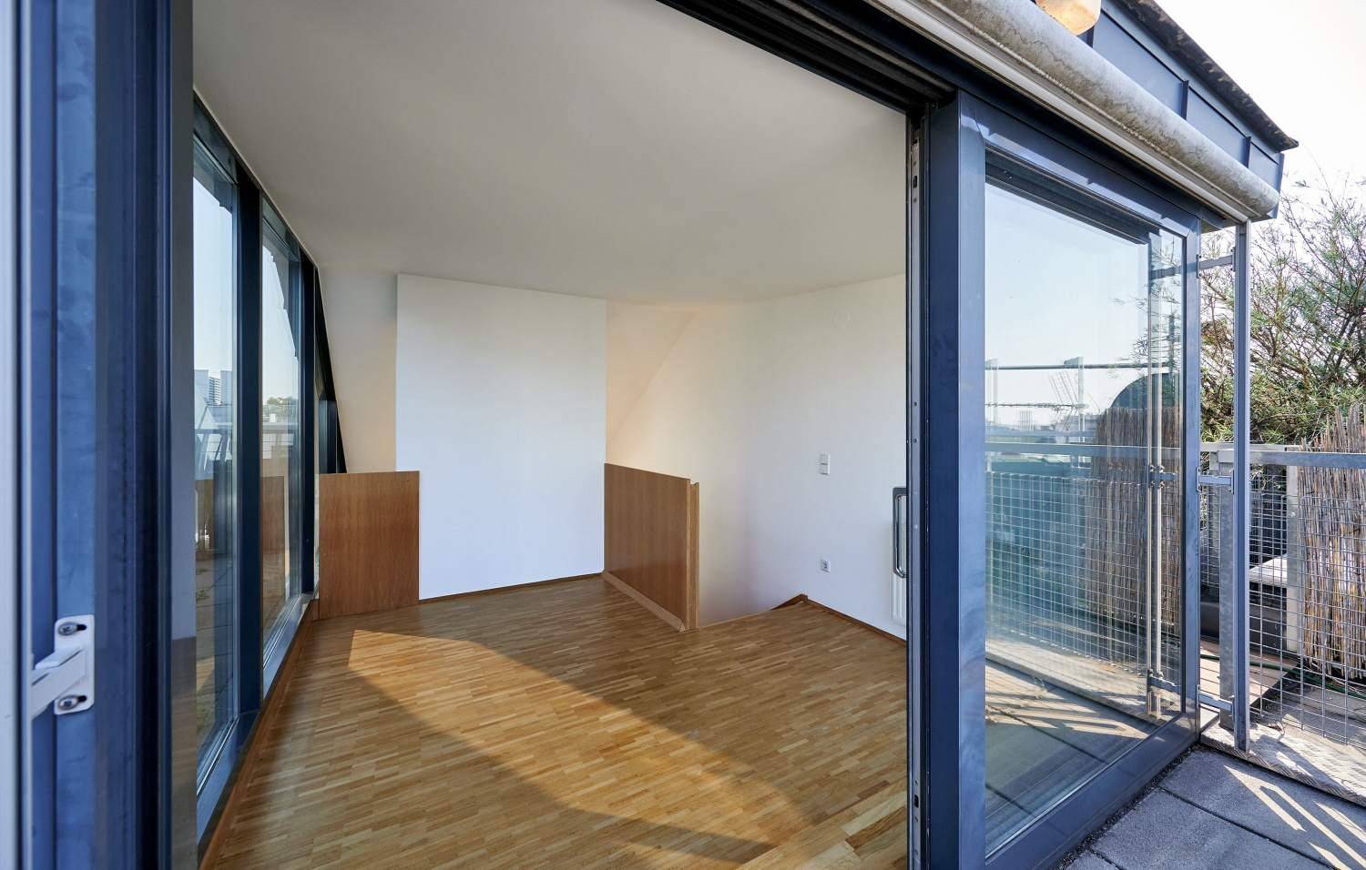 Heller Innenraum mit Holzfußboden und großen Glasfronten, die viel Licht hereinlassen.