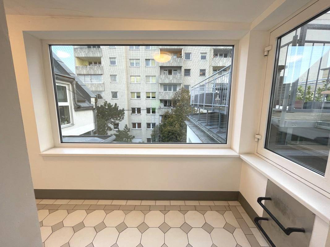 Heller Flur mit großem Fenster und Blick auf gegenüberliegende Gebäude.
