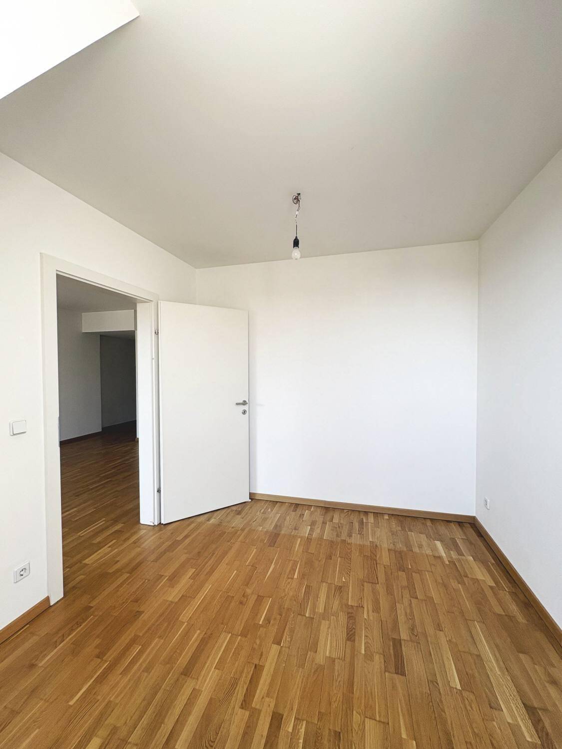 Geräumiges Schlafzimmer mit hellem Parkettboden und weiß gestrichenen Wänden.