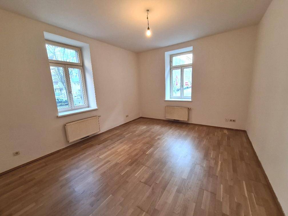 Geräumiges Schlafzimmer mit Parkettboden und viel Tageslicht durch zwei Fenster.