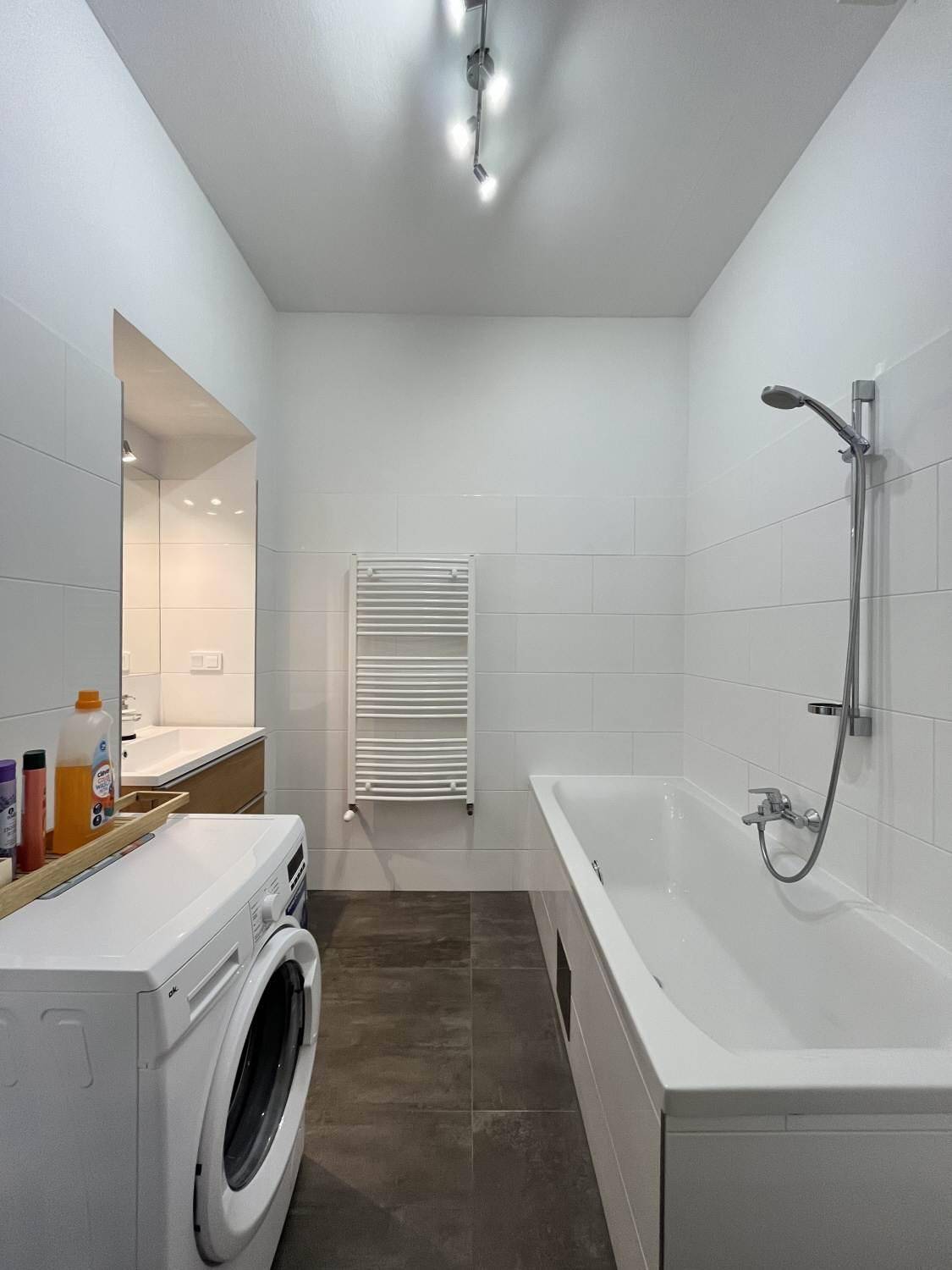 Modernes Badezimmer mit Badewanne, integrierter Dusche, Waschmaschine und weiß gefliesten Wänden.