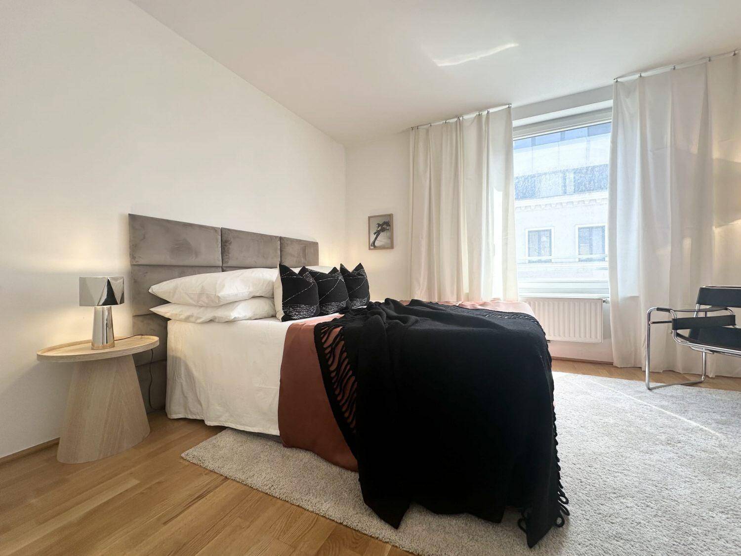 Helles Schlafzimmer mit Doppelbett, Holzboden und großen Fenstern für viel Licht.