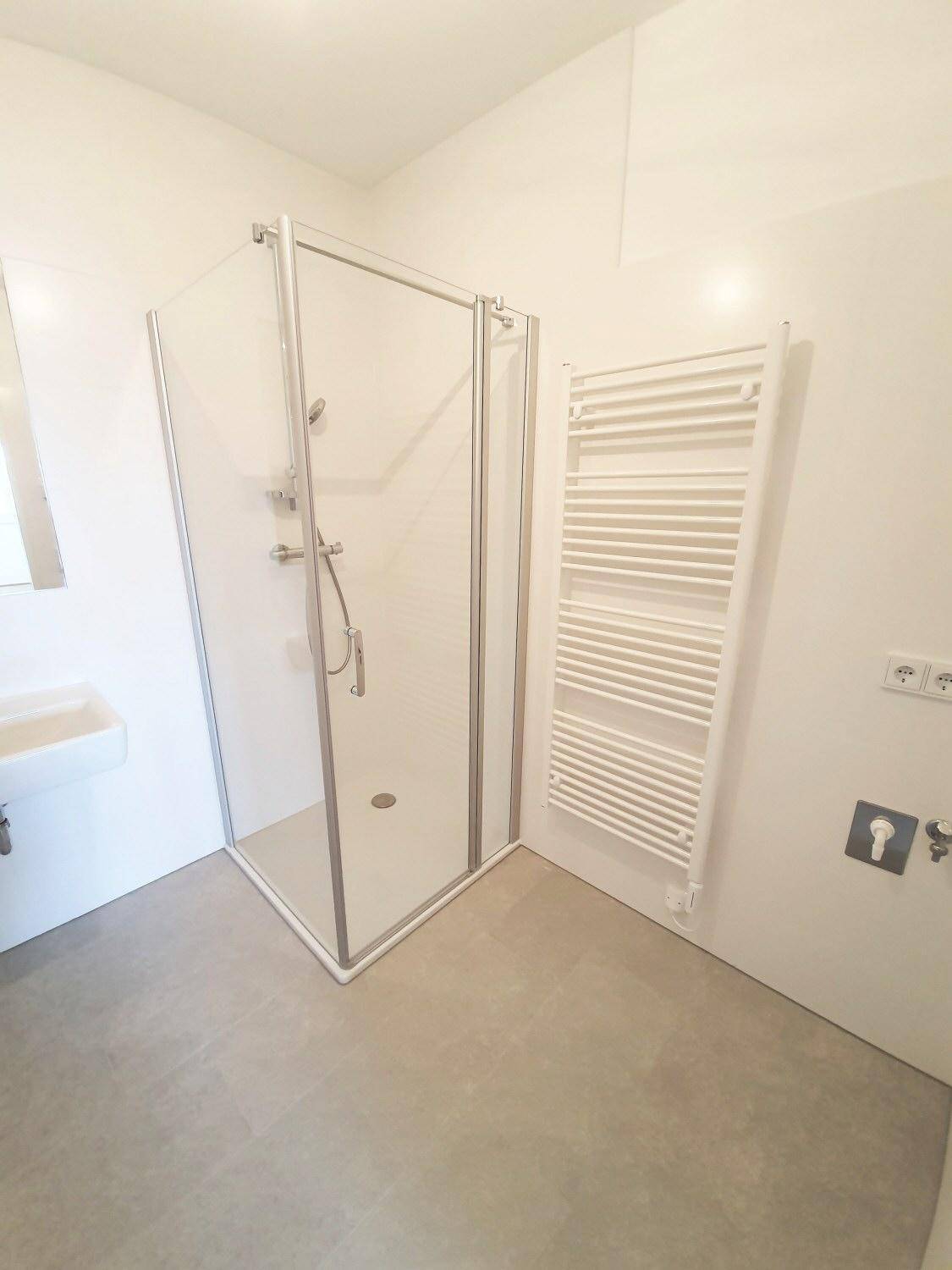 Modernes Badezimmer mit Duschkabine aus Glas, beheiztem Handtuchhalter und hellgrauen Fliesen.