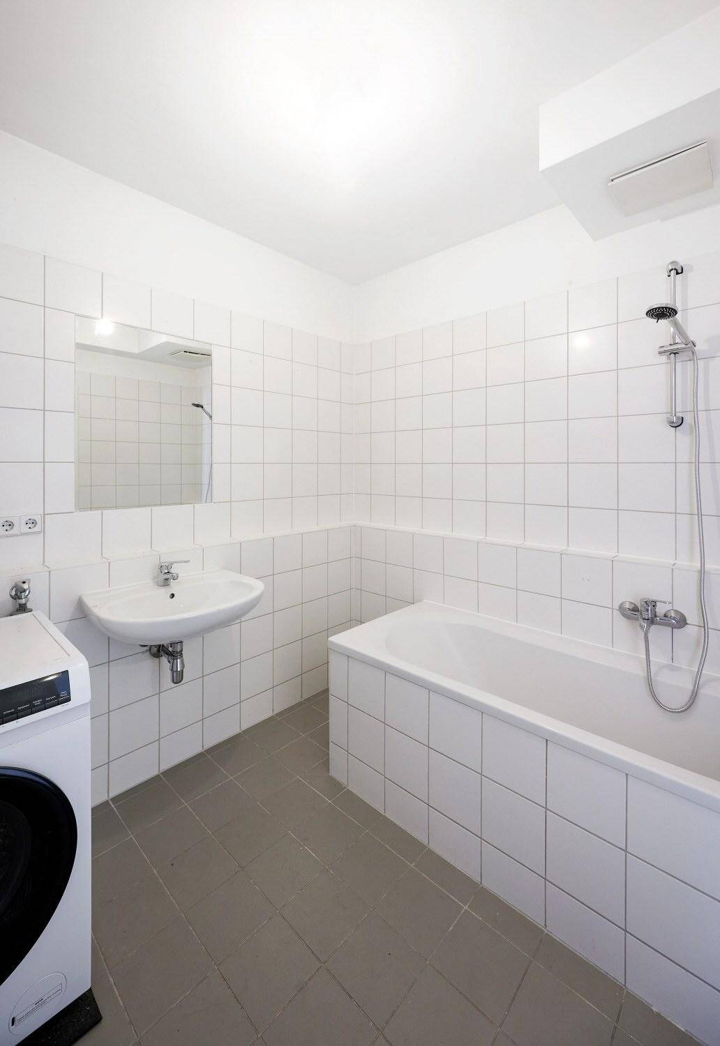 Helles Badezimmer mit Badewanne, Waschbecken und Waschmaschine, komplett gefliest.
