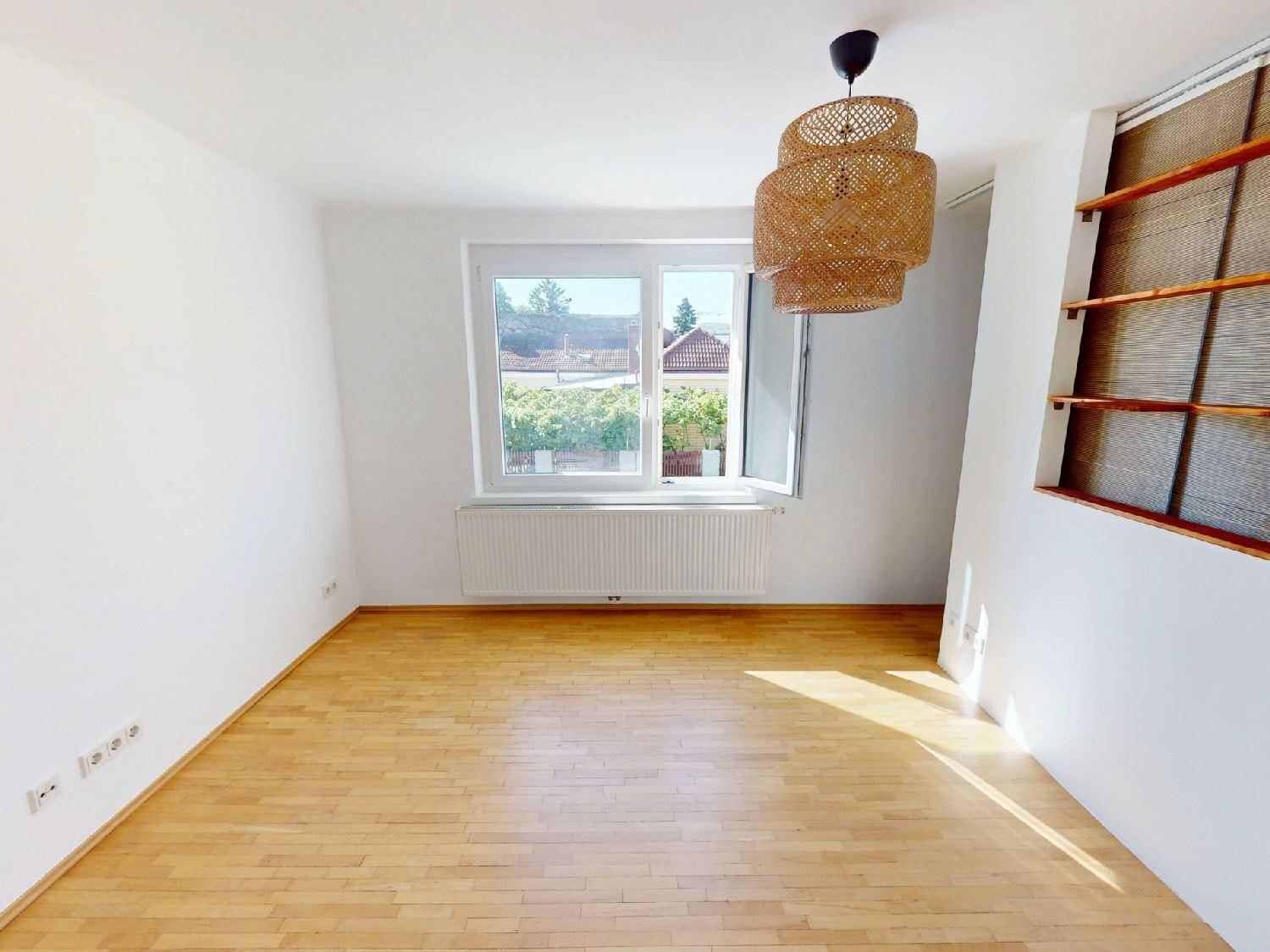 Helles Zimmer mit Parkettboden, großem Fenster und dekorativer Deckenleuchte.