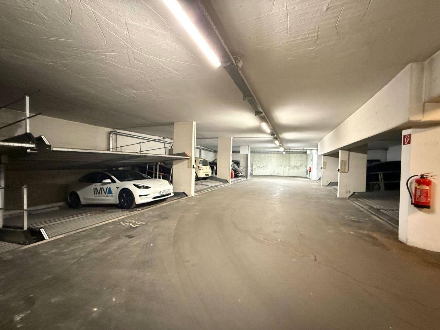 Geräumige Tiefgarage mit Betonwänden, Leuchtstoffröhren und Doppelparkern für Fahrzeuge.
