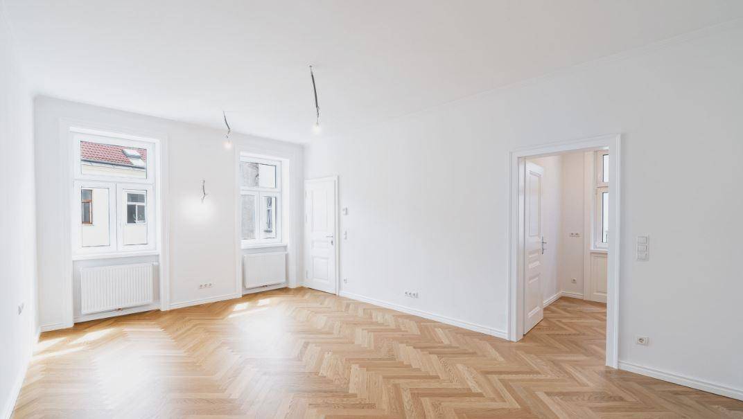 Geräumiges Wohnzimmer mit elegantem Fischgrätparkett und Zugang zu weiteren Räumen.