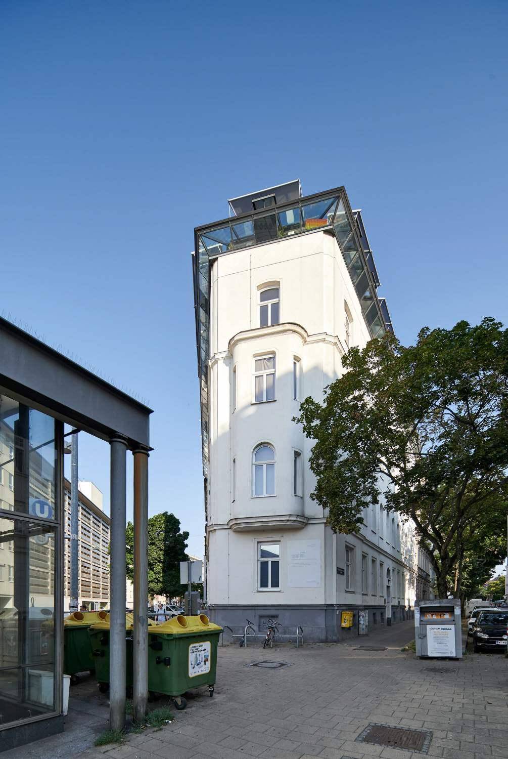Historisches Eckgebäude mit moderner Dachaufstockung und klarem Himmel.