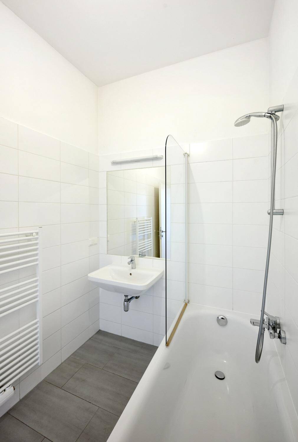 Helles Badezimmer mit Badewanne, Duschvorrichtung, Waschbecken und beheiztem Handtuchhalter.