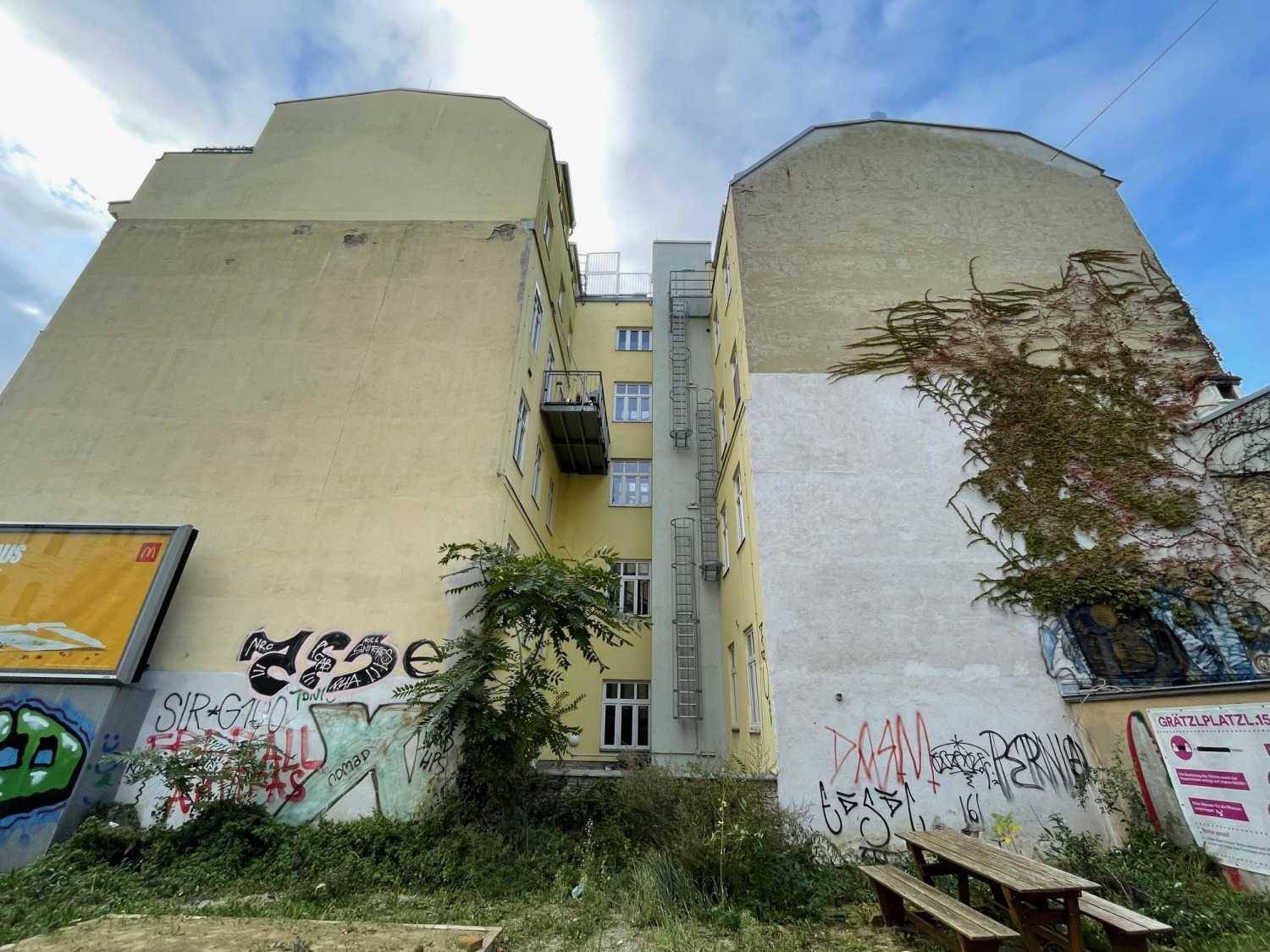 Hinterhofansicht zwischen Gebäuden mit Graffiti, Grünflächen und einem Balkon.