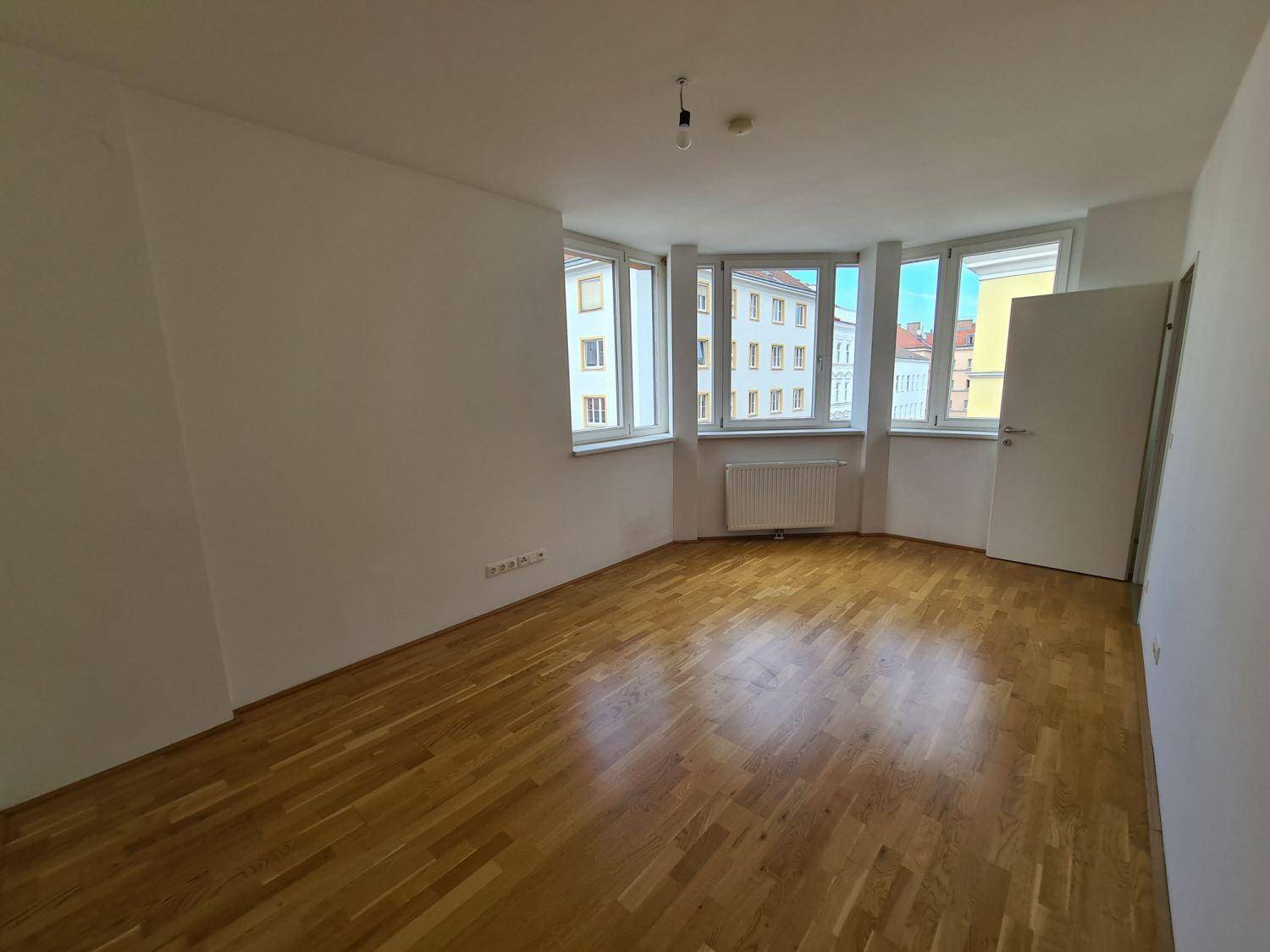 Helles Zimmer mit Parkettboden und vielen Fenstern, die einen Stadtblick bieten.