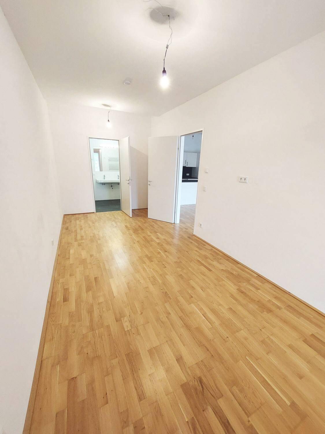 Heller Raum mit Parkettboden und offenen Zugängen zu Bad und Küche, ideal für eine flexible Nutzung.