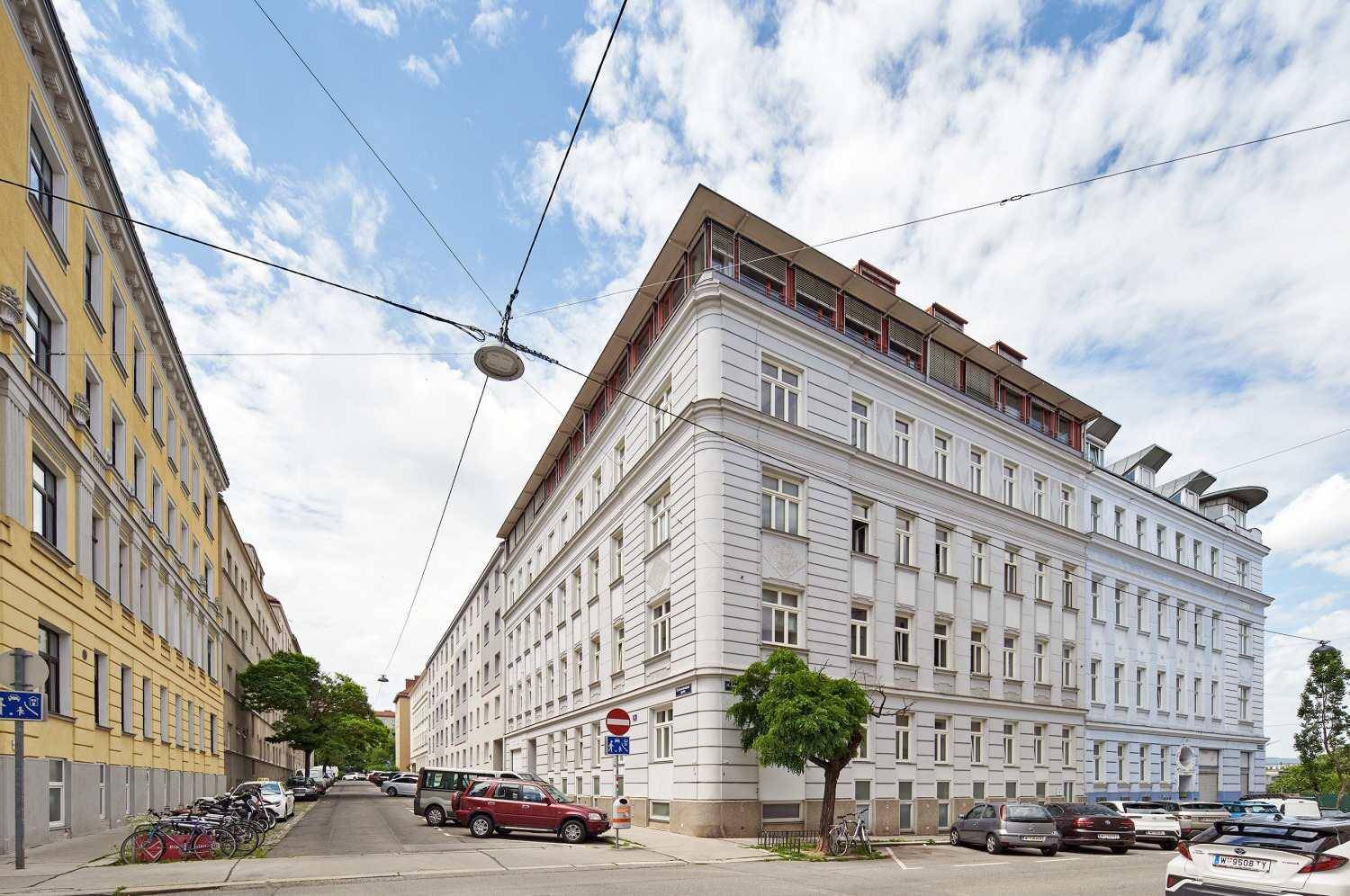 Weitläufige Ansicht des Eckgebäudes in einer belebten Stadtstraße mit Parkplätzen.