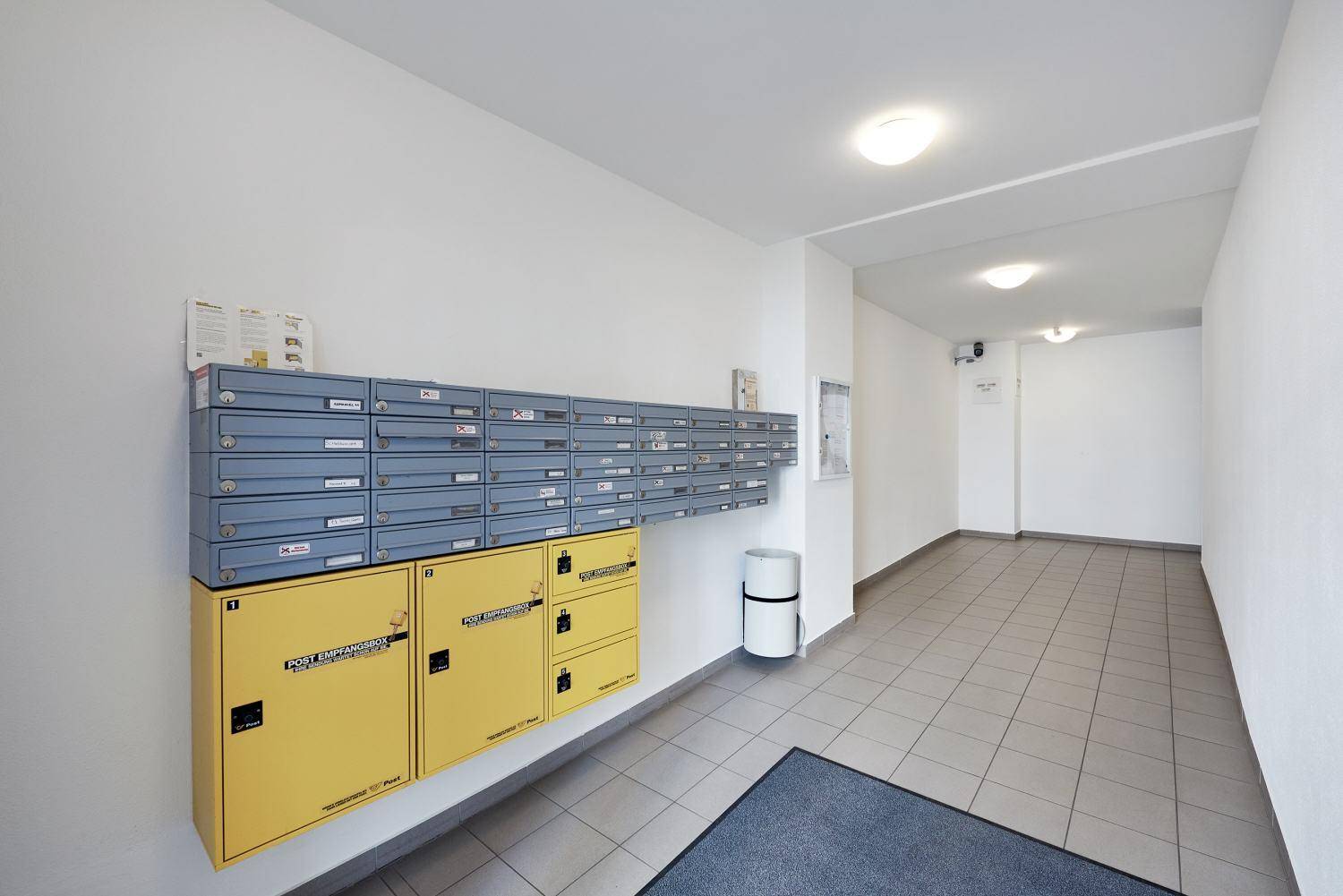 Heller Eingangsbereich eines Wohnhauses mit Briefkästen und einem gefliesten Boden.