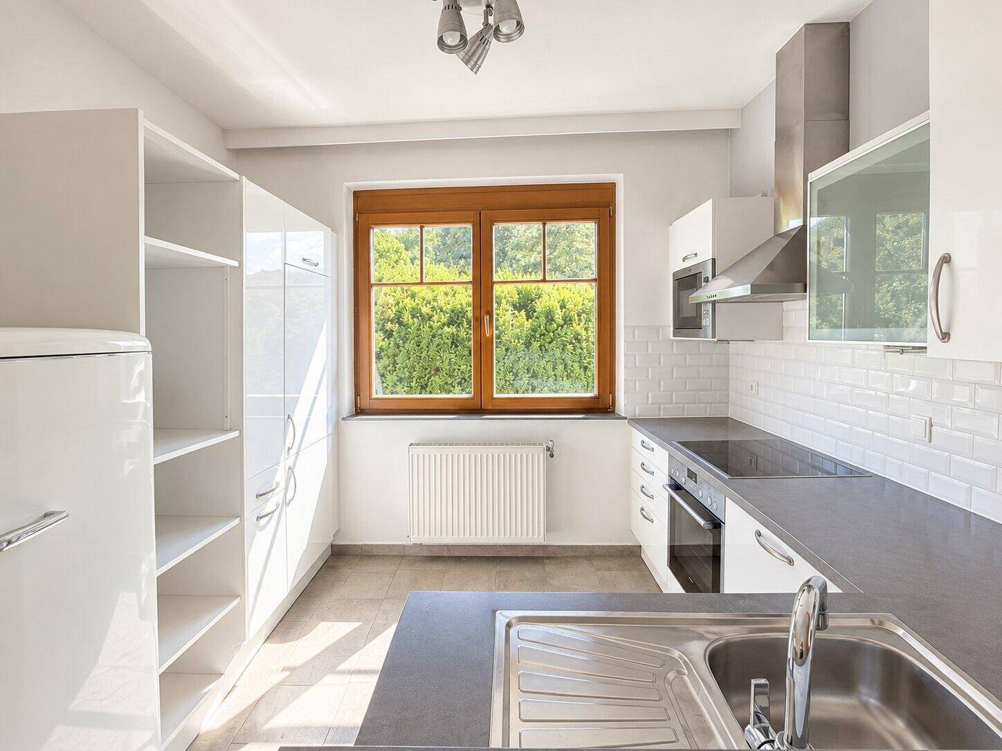 Moderne Einbauküche mit weißen Hochglanzfronten, Induktionskochfeld und integriertem Kühlschrank.