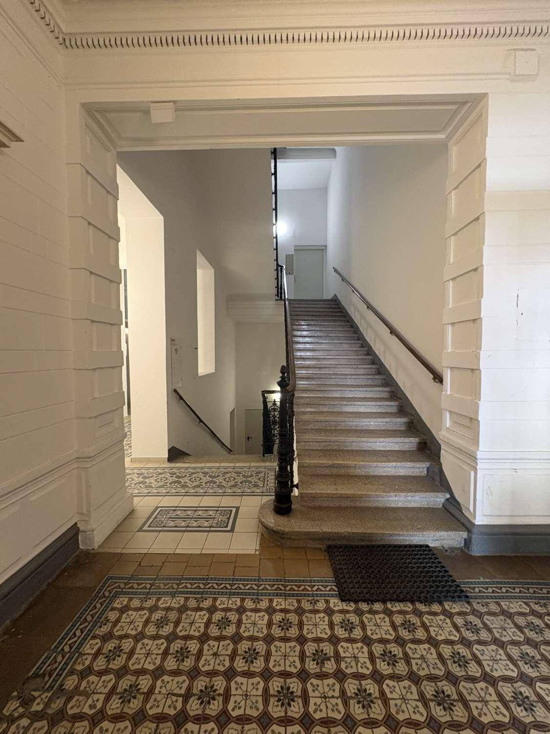 Prunkvolle Eingangshalle mit breiter Steintreppe, kunstvollem Geländer und gemusterten Fliesenböden, Altbau-Charme.