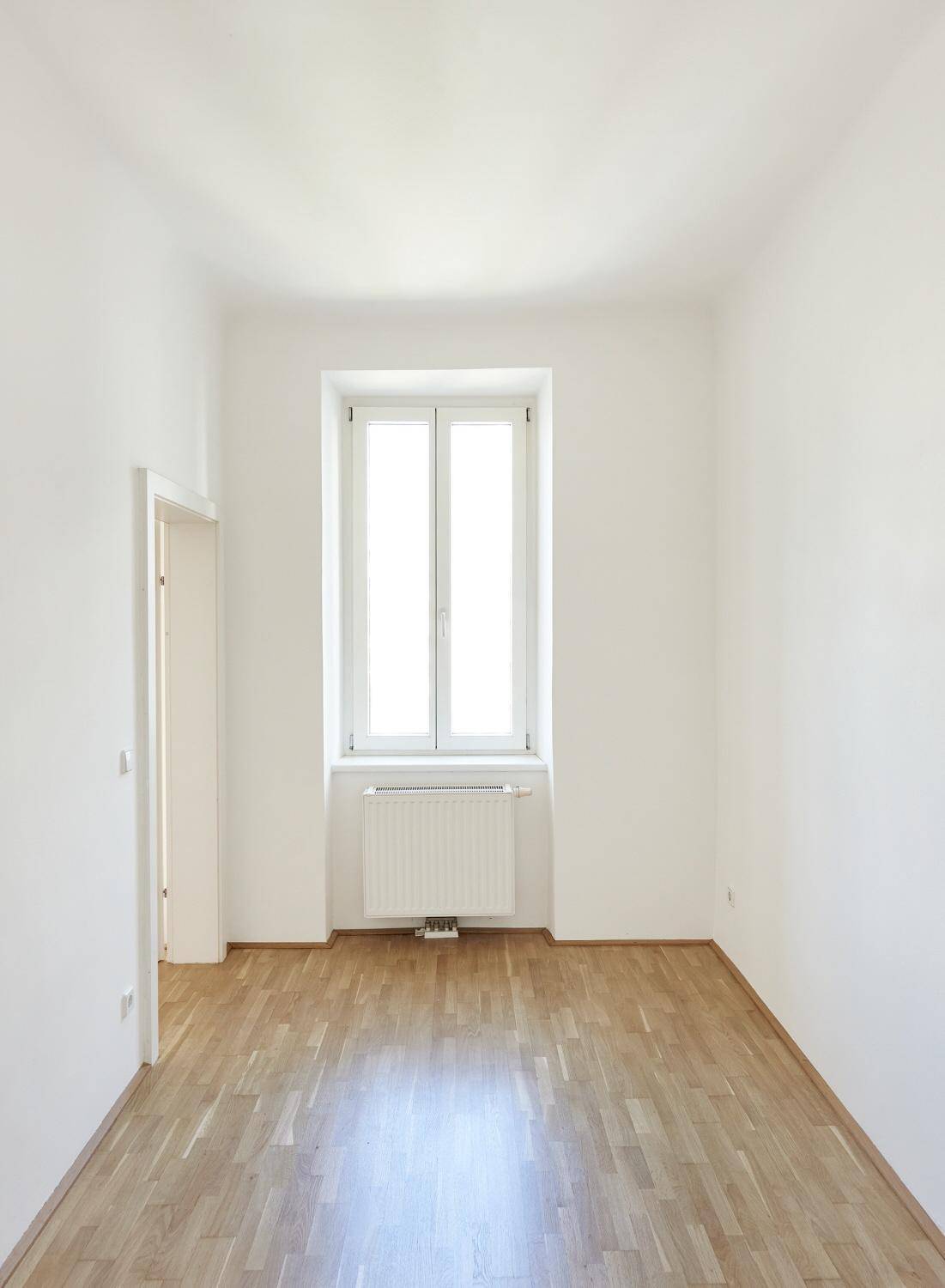Heller, leerer Raum mit Parkettboden und großem Fenster, ideal für verschiedene Nutzungen.