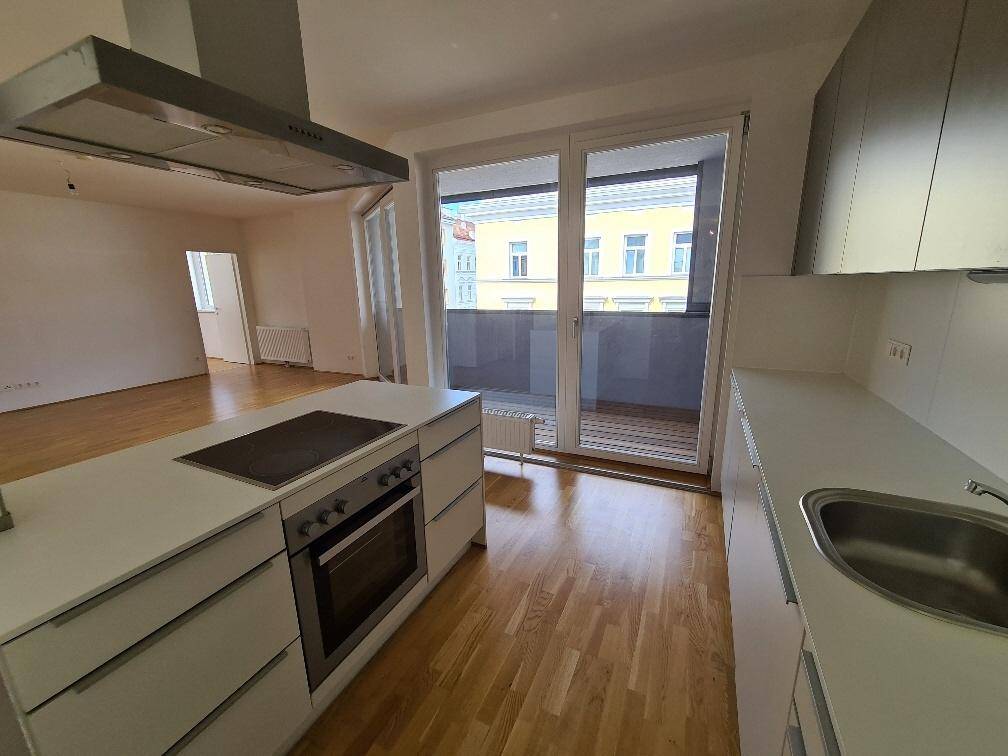 Küchenbereich mit Kochinsel und Blick durch die großen Fenster auf den Balkon und die Stadt.