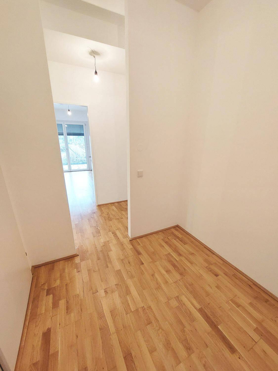 Eingangsbereich mit Parkettboden und hellem Durchgang zu einem weiteren Zimmer mit Terrassenzugang.