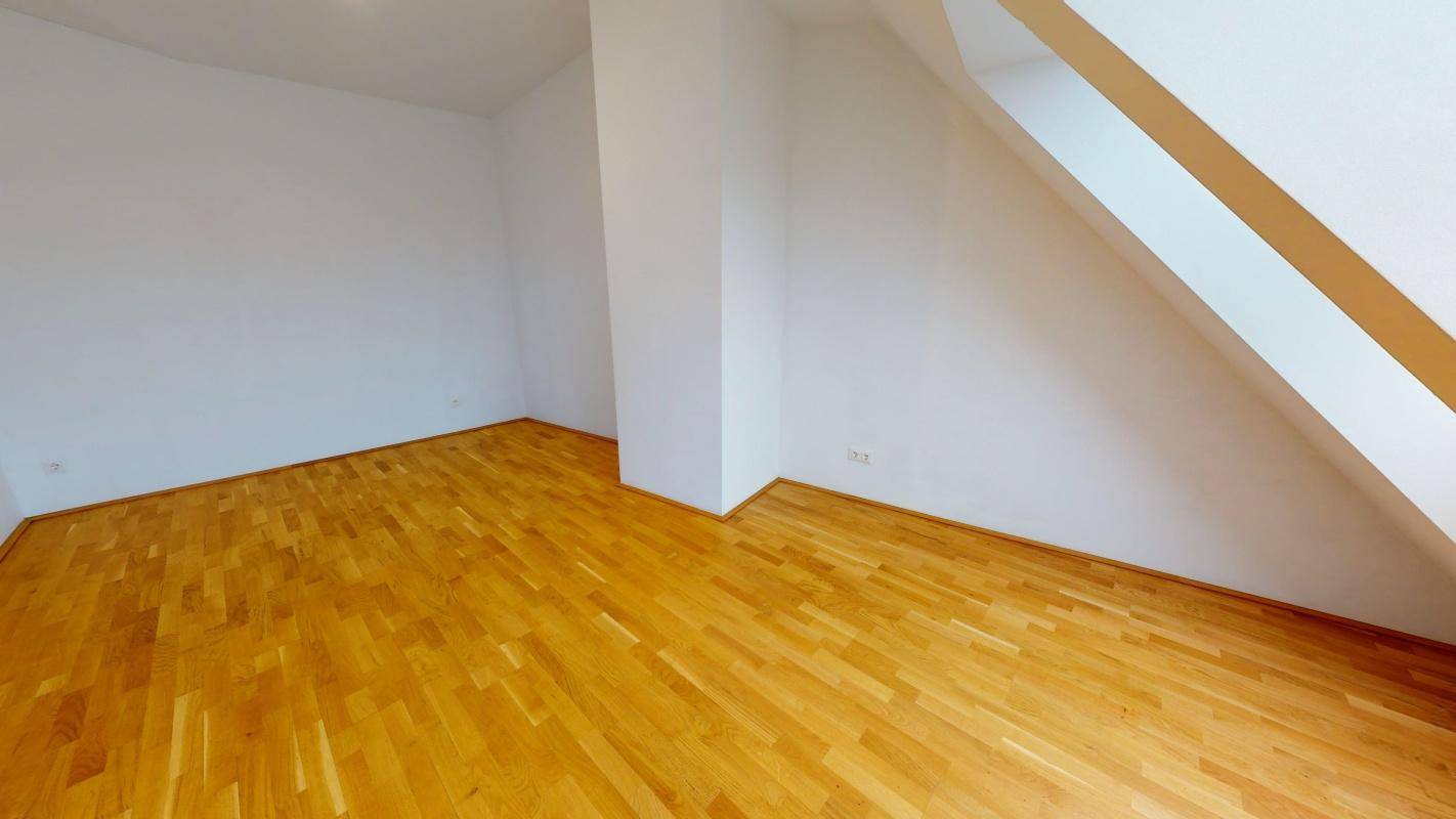 Geräumiger Dachgeschossraum mit Holzboden und schrägen Wänden, vielseitig nutzbar.