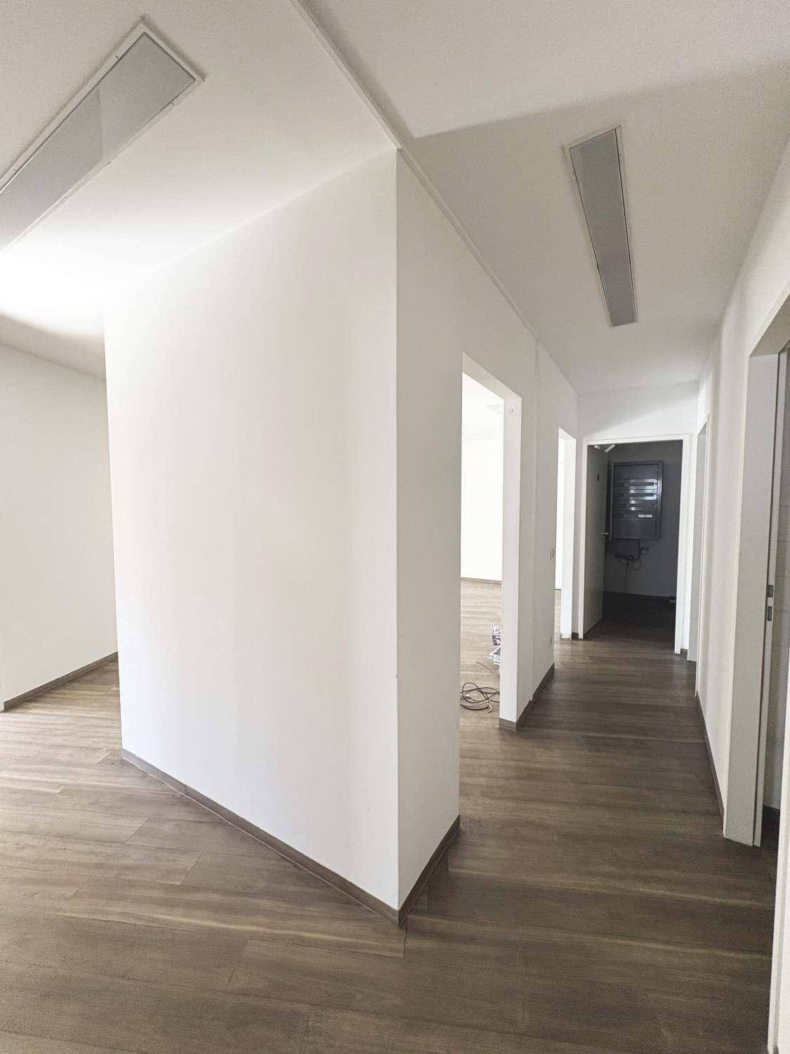 Langer Flur mit Holzboden, weißen Wänden und mehreren Türen zu angrenzenden Räumen.