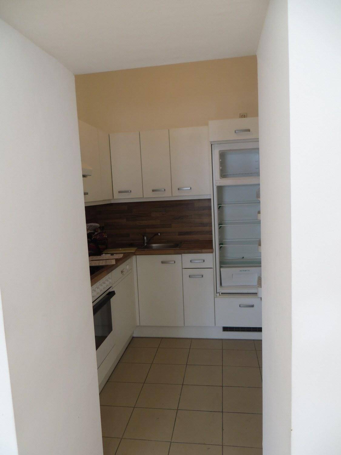 Kompakte Küche mit weißen Schränken, Fliesenboden und integriertem Kühlschrank.