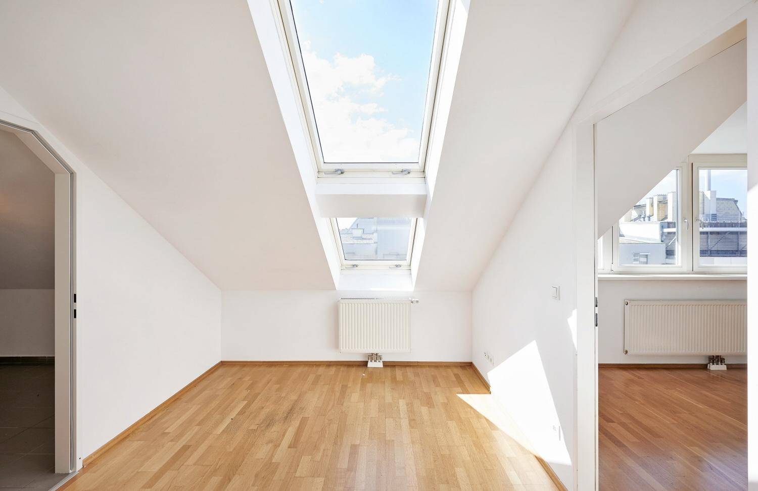 Dachgeschossraum mit Holzboden, schrägen Wänden und zwei großen Dachfenstern für viel Licht.