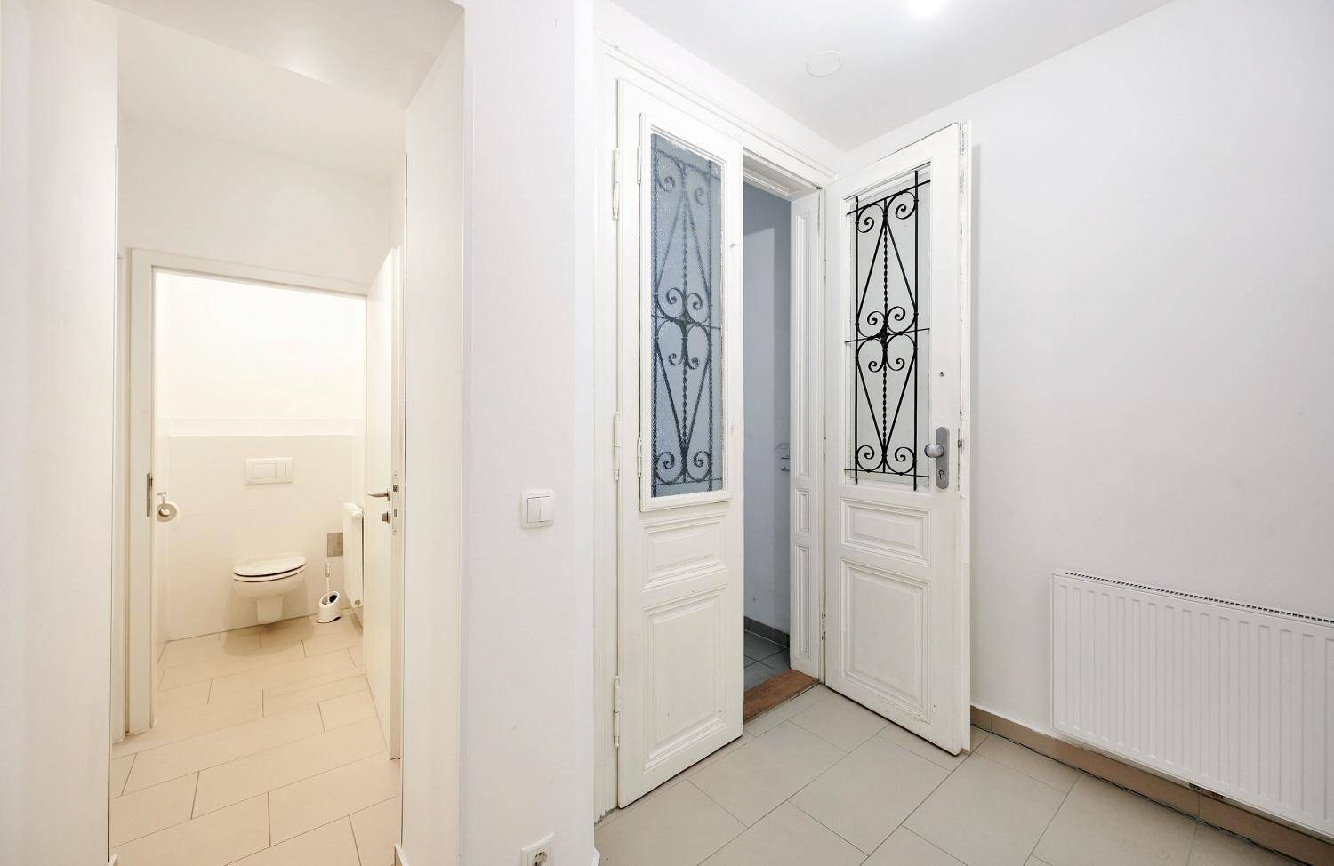 Eingangsbereich mit gefliestem Boden, dekorativer Tür und Blick in ein separates WC.